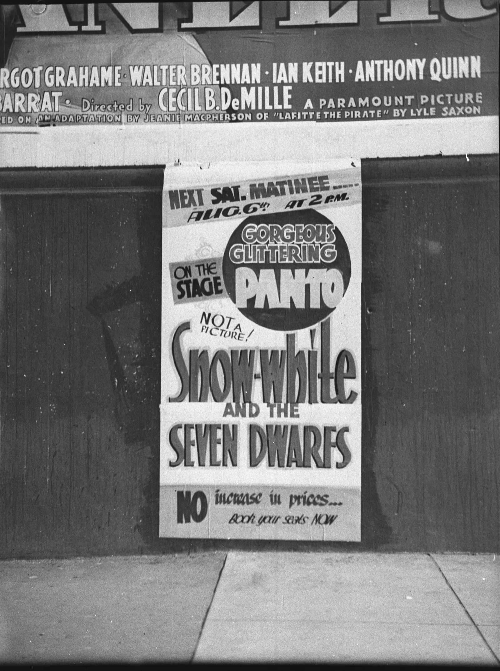 A hand-lettered show card pasted to a picture theatre’s wall: next Saturday’s matinee, August 6th at 2 p.m., on the stage, a gorgeous glittering panto, not a picture, Snow-white and the Seven Dwarfs, no increase in prices, book your seats now.
